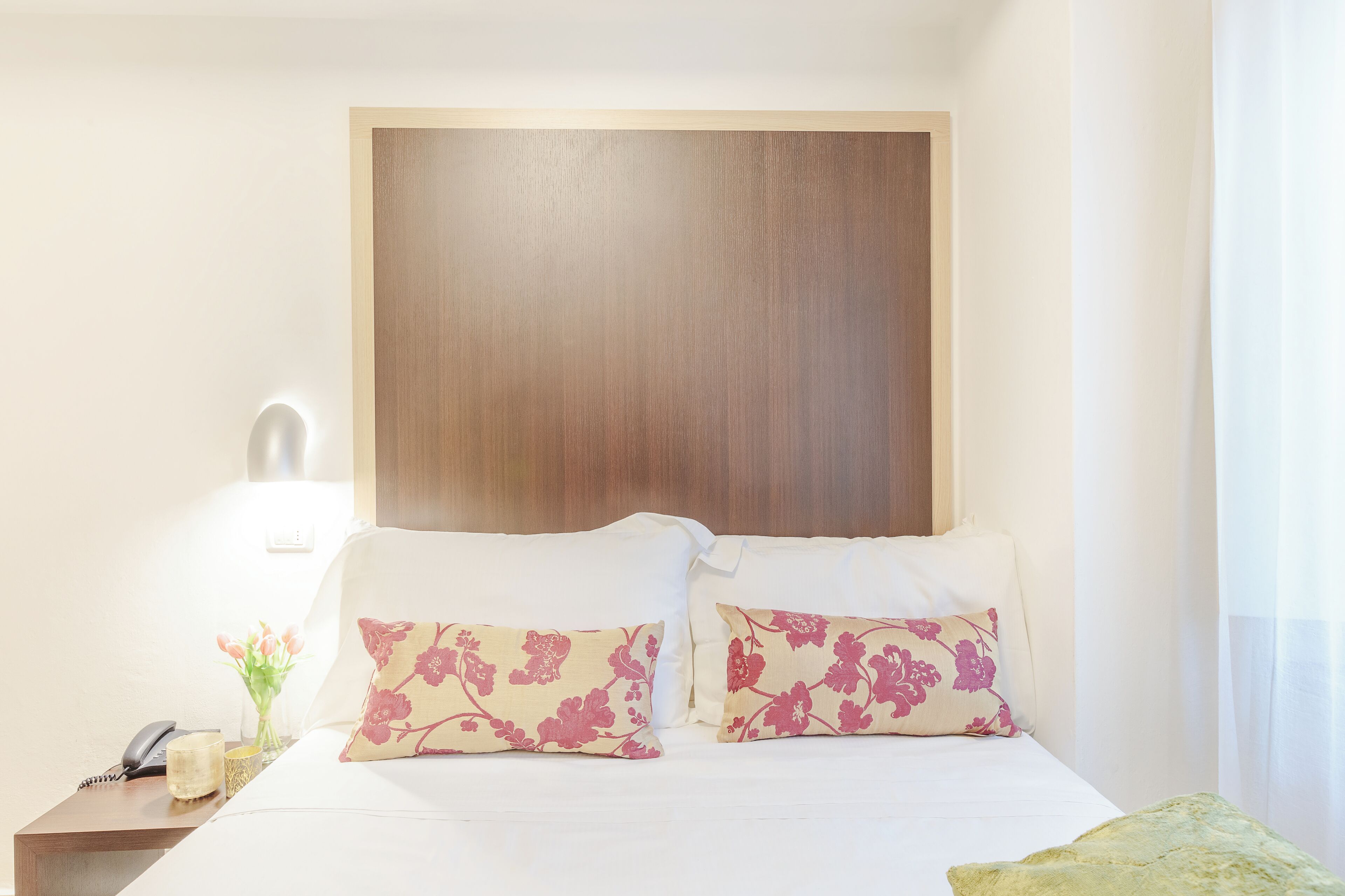A hotel room with a wooden headboard, white bedding, and two floral pillows.