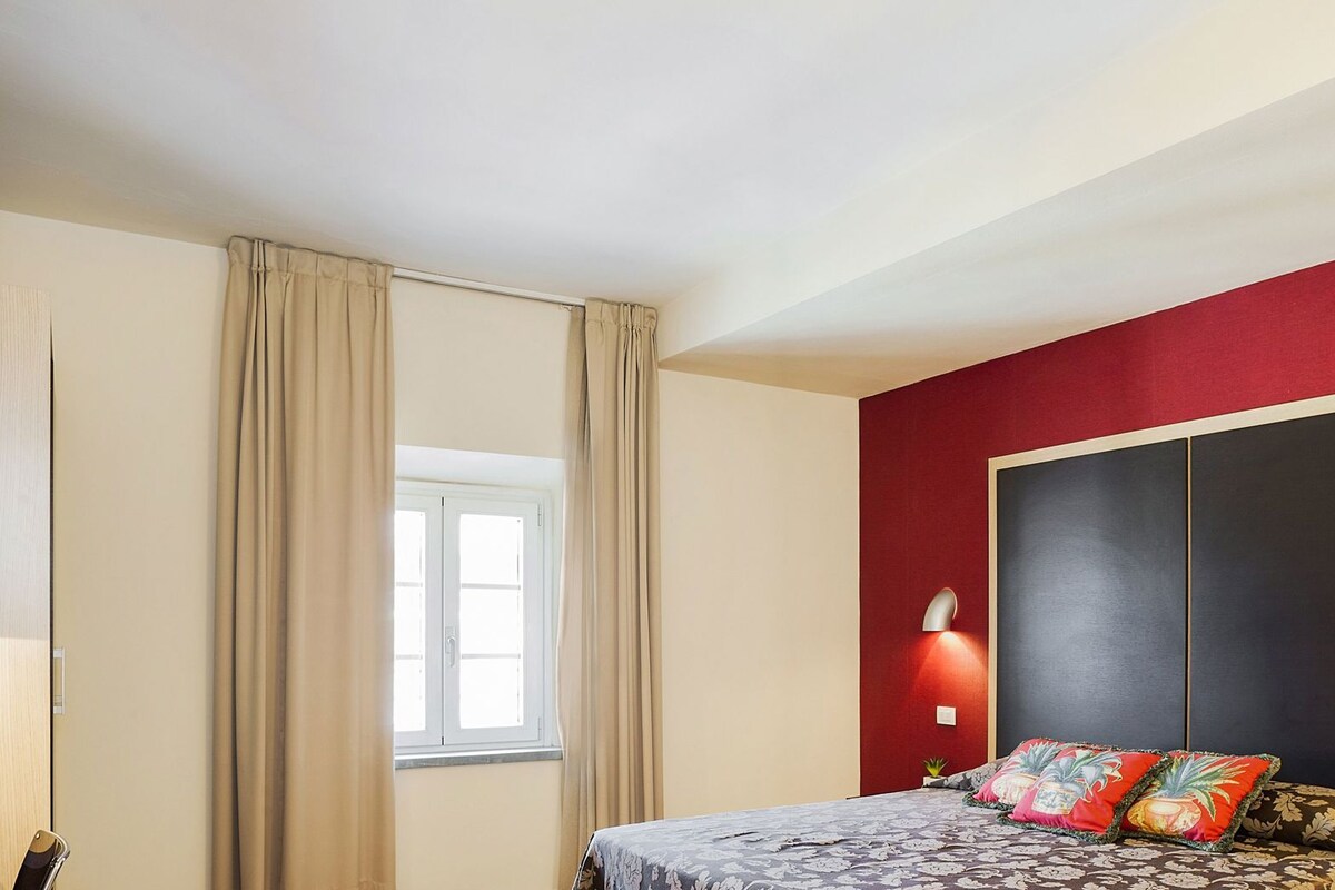Ein Schlafzimmer mit Bett, Vorhängen, einem Fenster, einem Schrank und Wandleuchten.