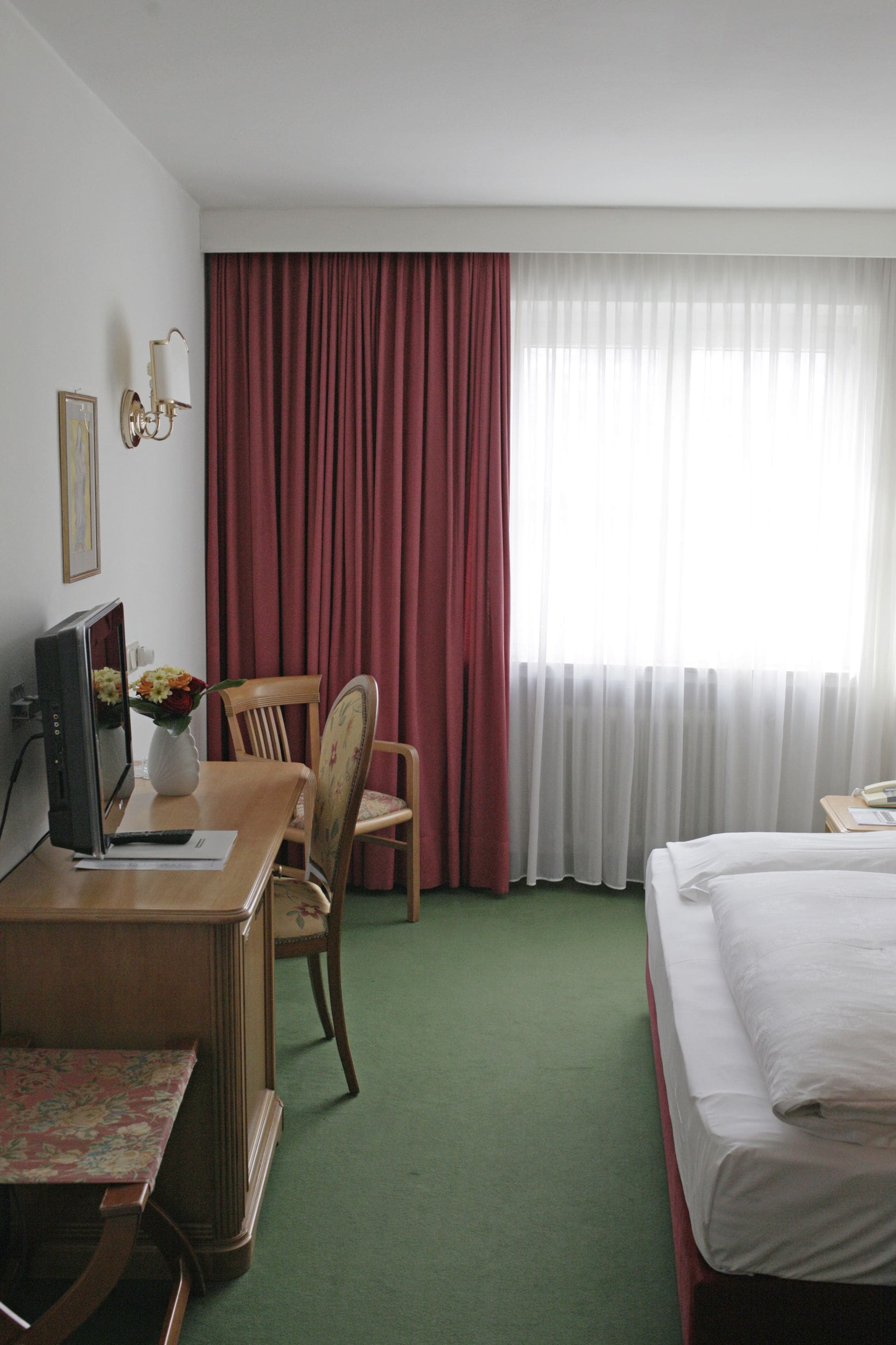 A hotel room with a desk, chair, bed, and curtains.