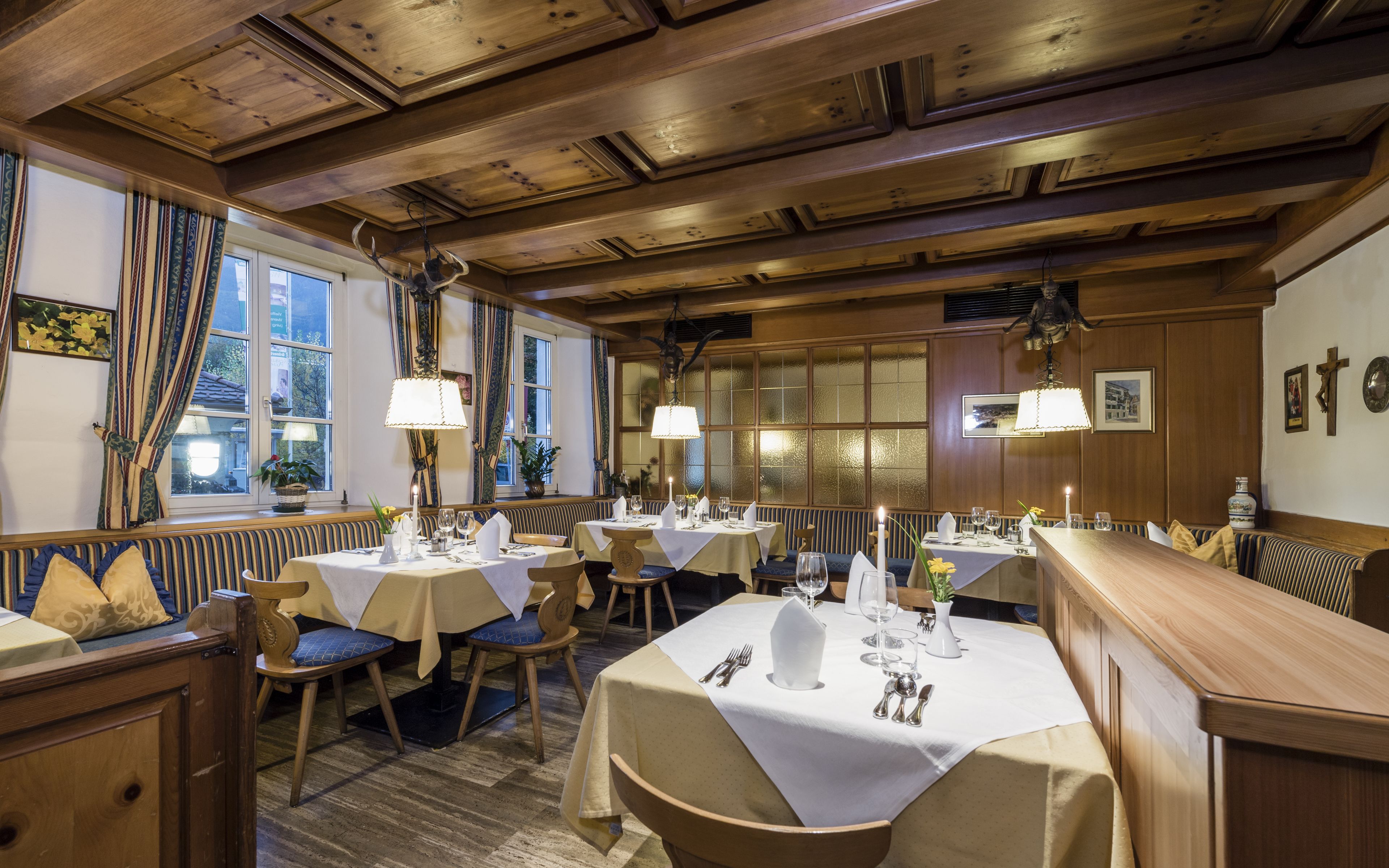 A restaurant with wooden ceiling beams, tables set with white tablecloths, and blue cushioned chairs.