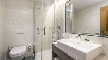 A modern bathroom with a glass-enclosed shower, a white sink, and a toilet.