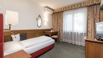 Une chambre d’hôtel comprenant un lit, un bureau, une chaise, une télévision, une lampe, un miroir et une fenêtre avec des rideaux.