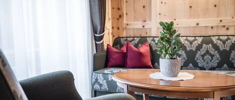 A cozy living area with a round wooden coffee table, a green sofa with floral cushions, and a potted plant.
