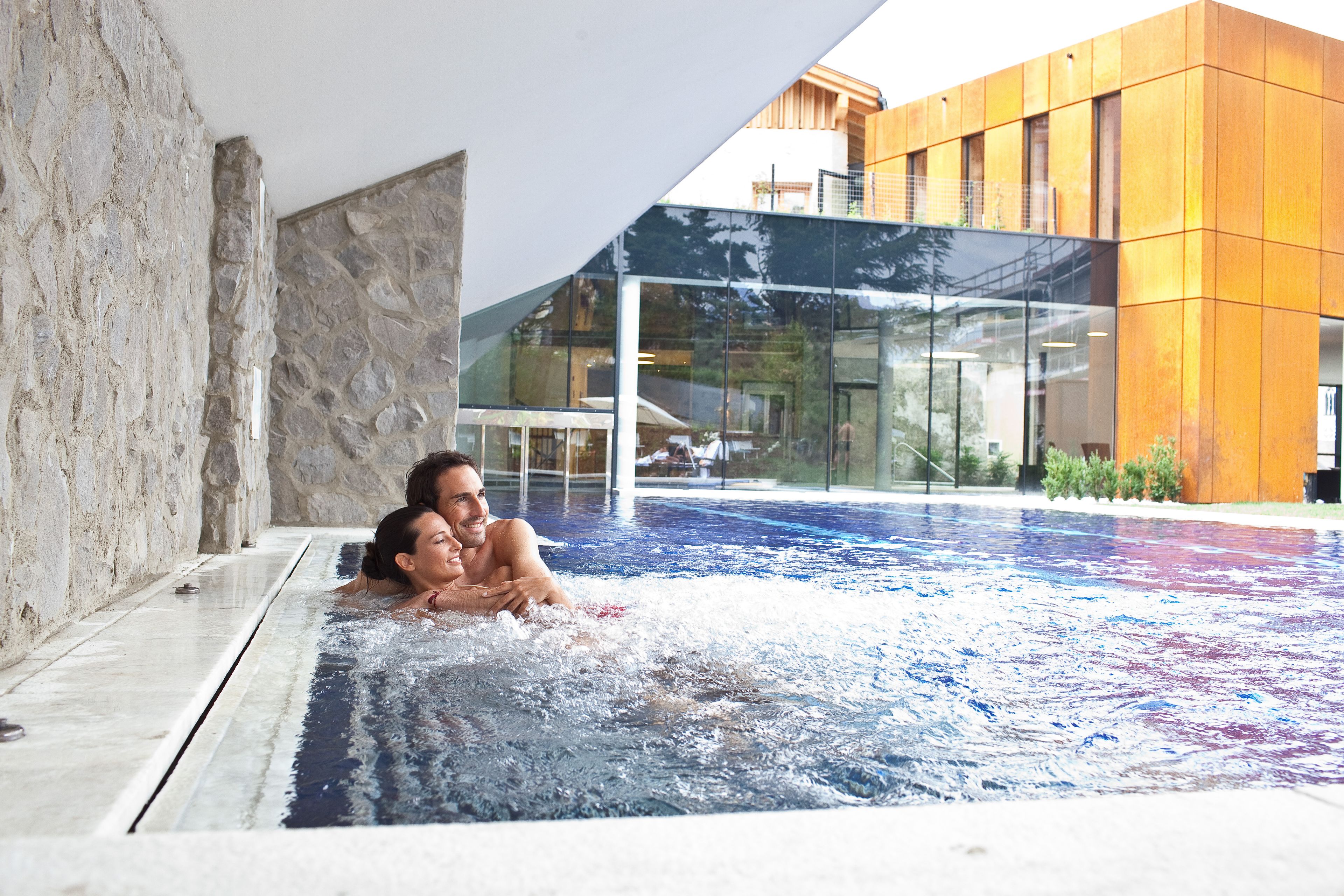 Una piscina interior moderna con agua cristalina, paredes de piedra y un edificio de vidrio al fondo.