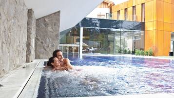 Una piscina interior moderna con agua cristalina, paredes de piedra y un edificio de vidrio al fondo.
