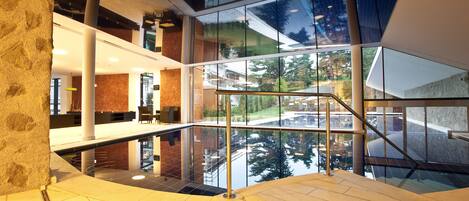 Un espacio interior moderno con suelo de vidrio que refleja los alrededores. Hay varios niveles con barandillas de vidrio y una escalera con barandillas de metal.