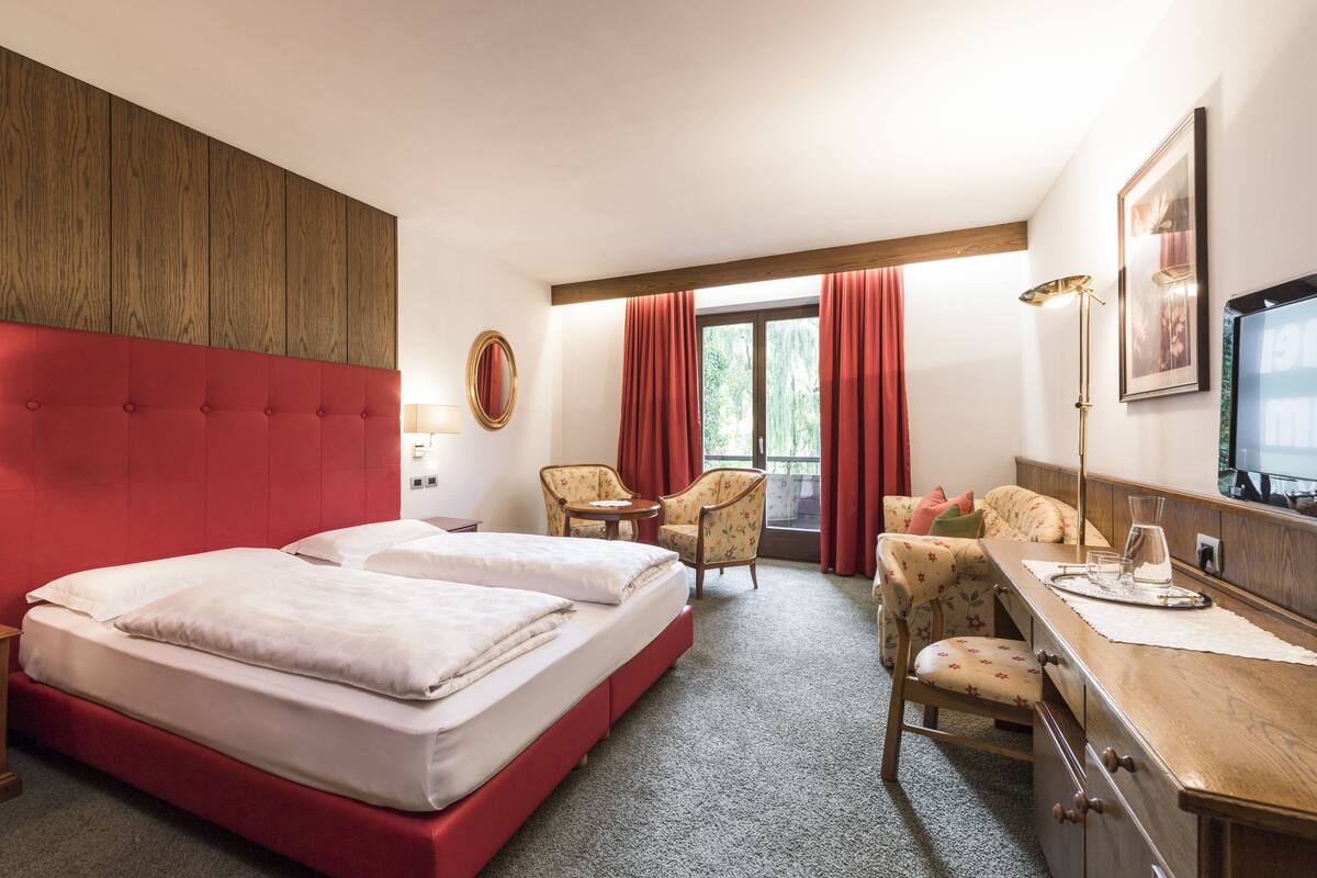 Habitación de hotel con una cama grande, dos sillones, un escritorio y una ventana con cortinas.