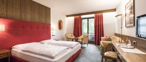 Habitación de hotel con una cama grande, dos sillones, un escritorio y una ventana con cortinas.