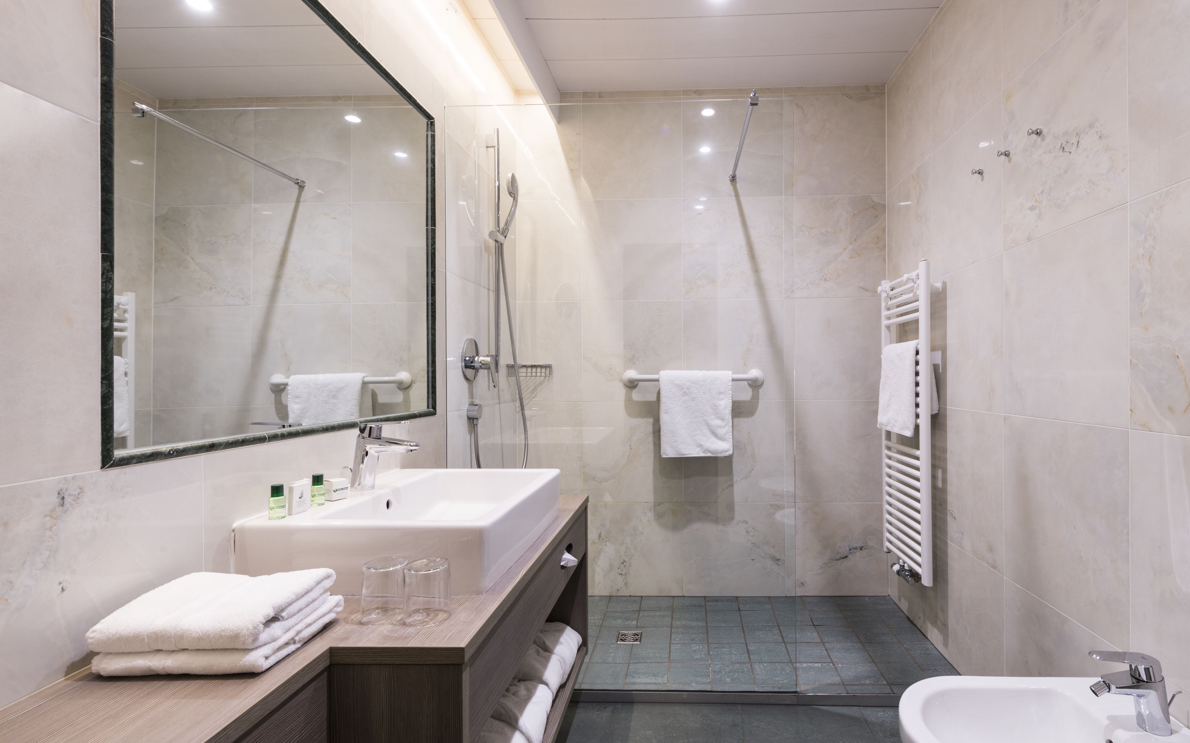 Un baño moderno con un espejo grande, un lavabo, una ducha y un inodoro.