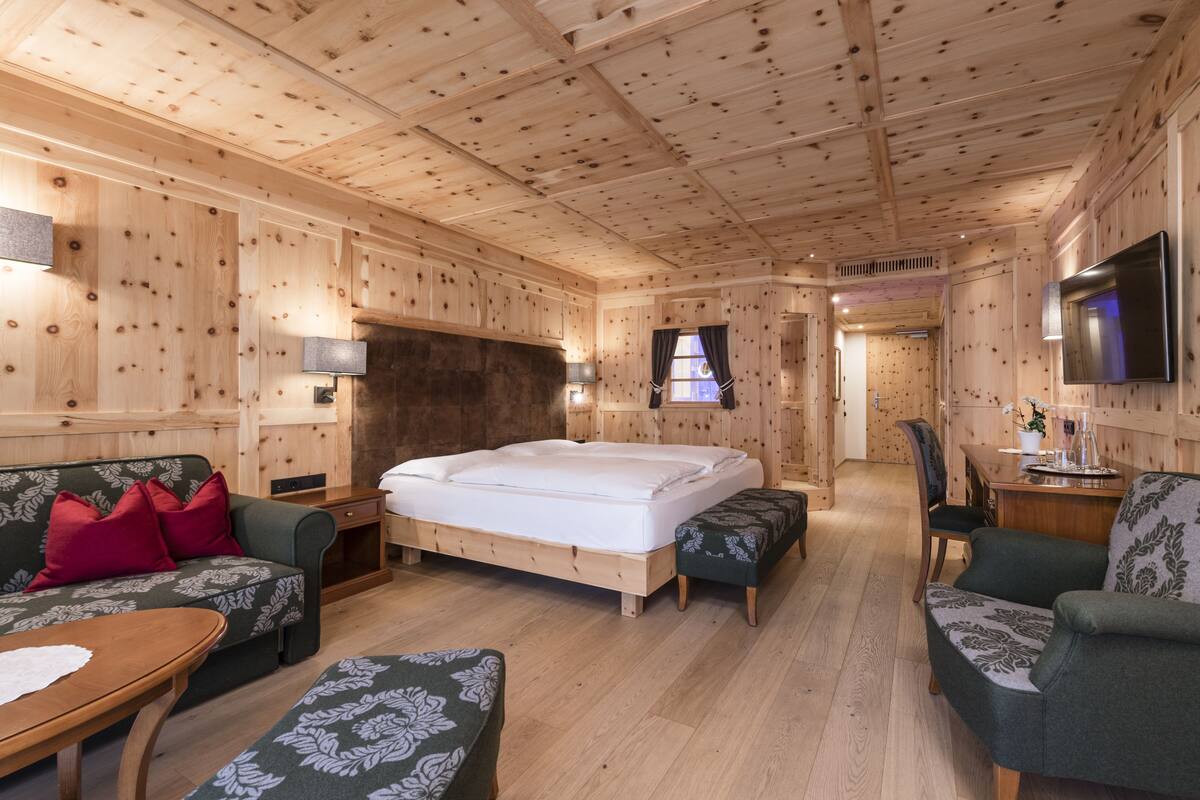 Un dormitorio tipo cabaña de madera con una cama, dos sofás tapizados en verde, una mesa de madera y un televisor en la pared.