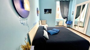 Un dormitorio con cama, una mesita, una silla y una ventana con cortinas.