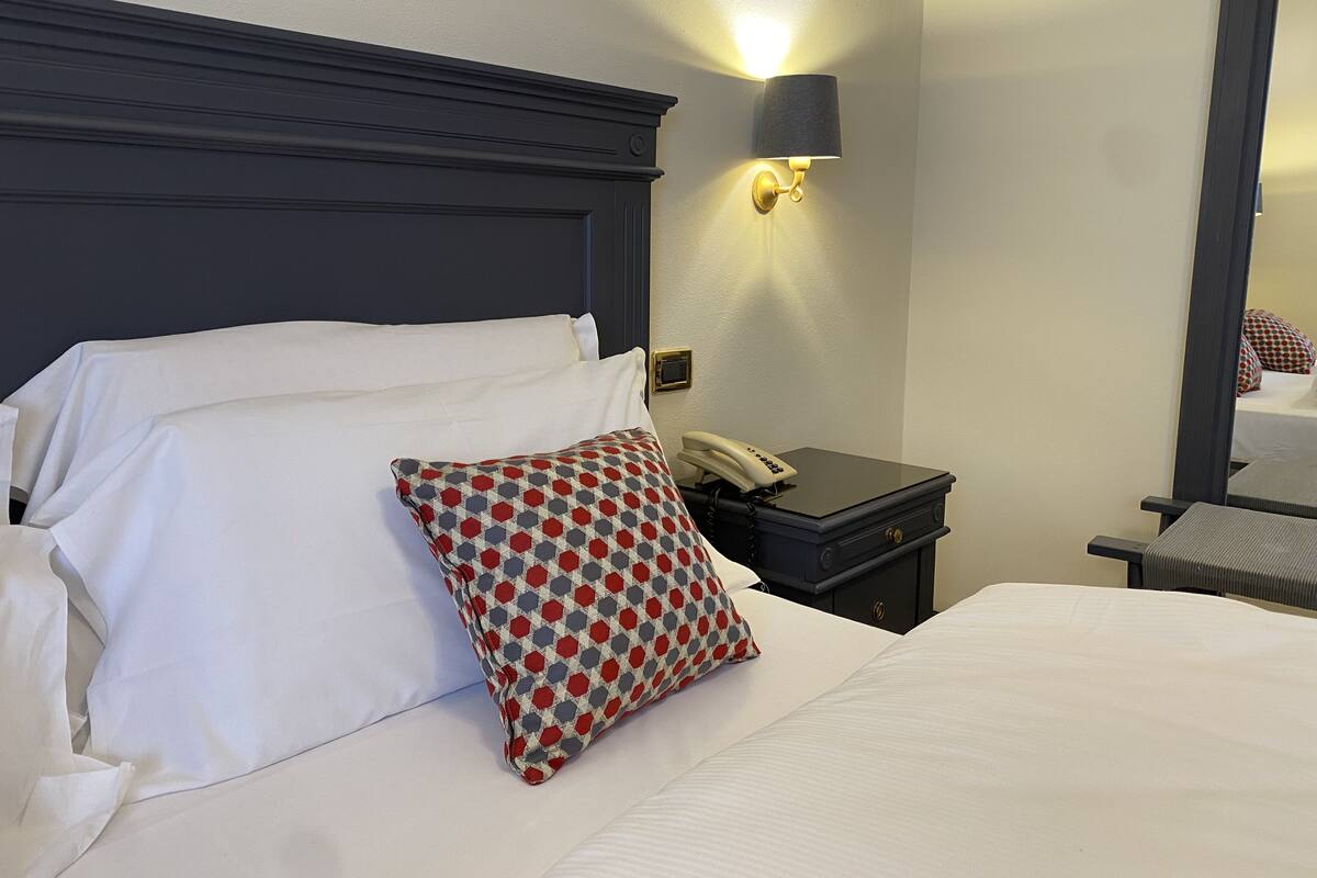 A hotel room with a large bed, a bedside table with a phone, a lamp, and a mirror.