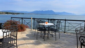 Terraço com mesa e cadeiras, vista para a água e montanhas.