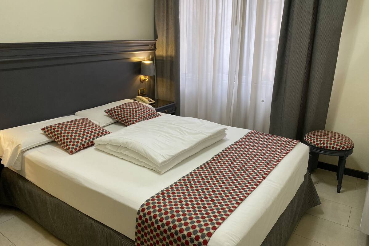 A neatly made bed with white linens and patterned pillows, a bedside lamp, and a telephone on a nightstand.