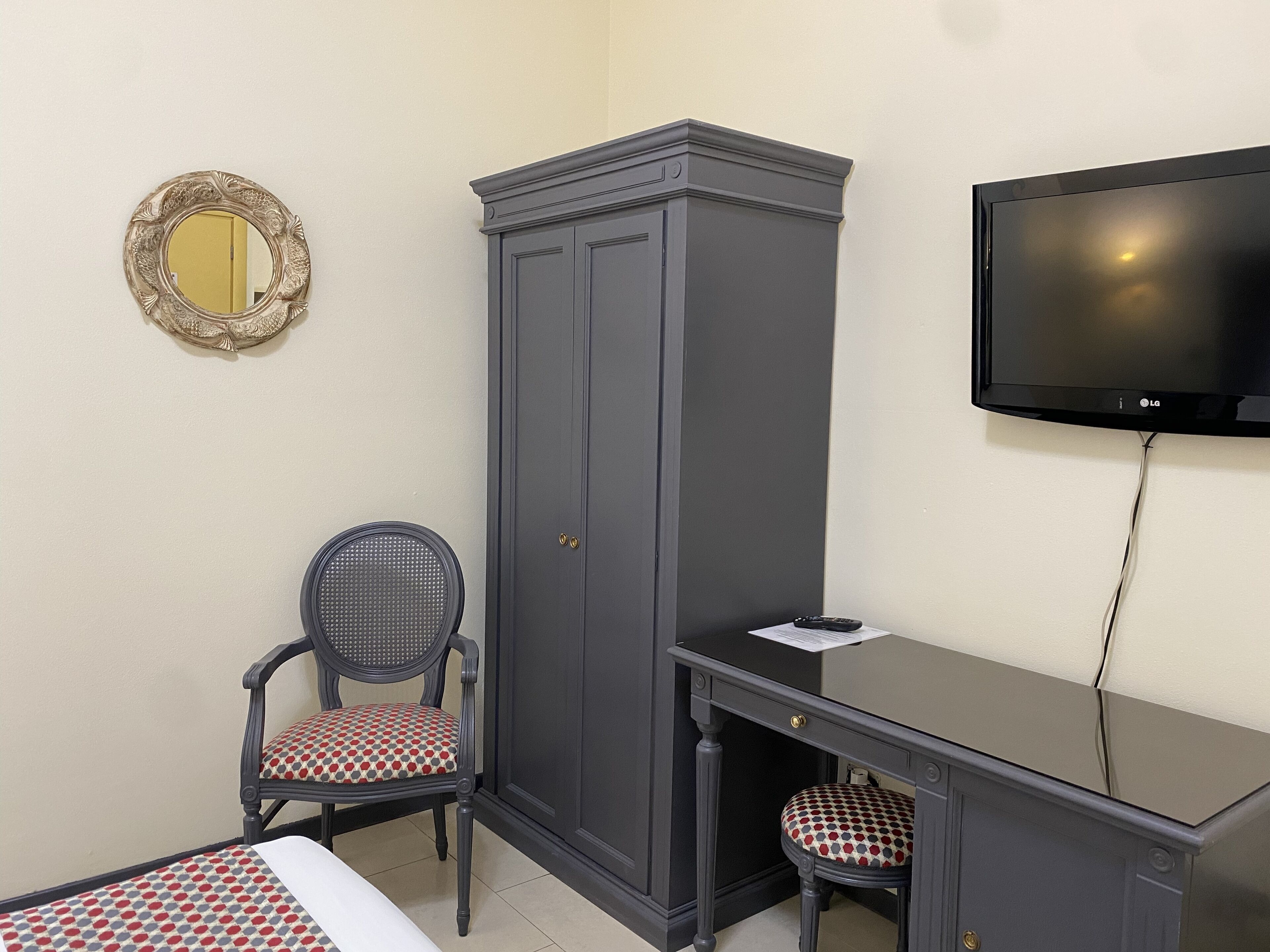 A room with a bed, a desk, a wardrobe, a chair, a television, and a mirror.
