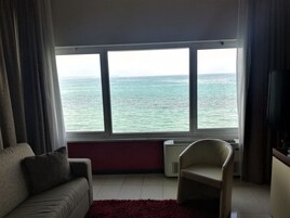 Un salón con un ventanal grande con vistas al mar, un sofá, un sillón y un radiador.