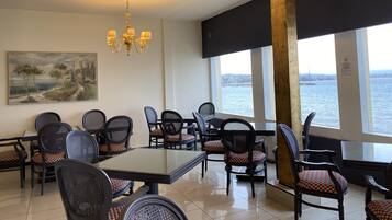Un comedor con vista al agua, que cuenta con una araña, un cuadro y una combinación de sillas modernas y clásicas.