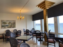 Un comedor con vista al agua, que cuenta con una araña, un cuadro y una combinación de sillas modernas y clásicas.