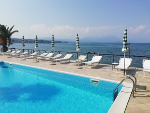Zona junto a la piscina con sillones de descanso y sombrillas, con vistas a una extensión de agua y montañas en la distancia.