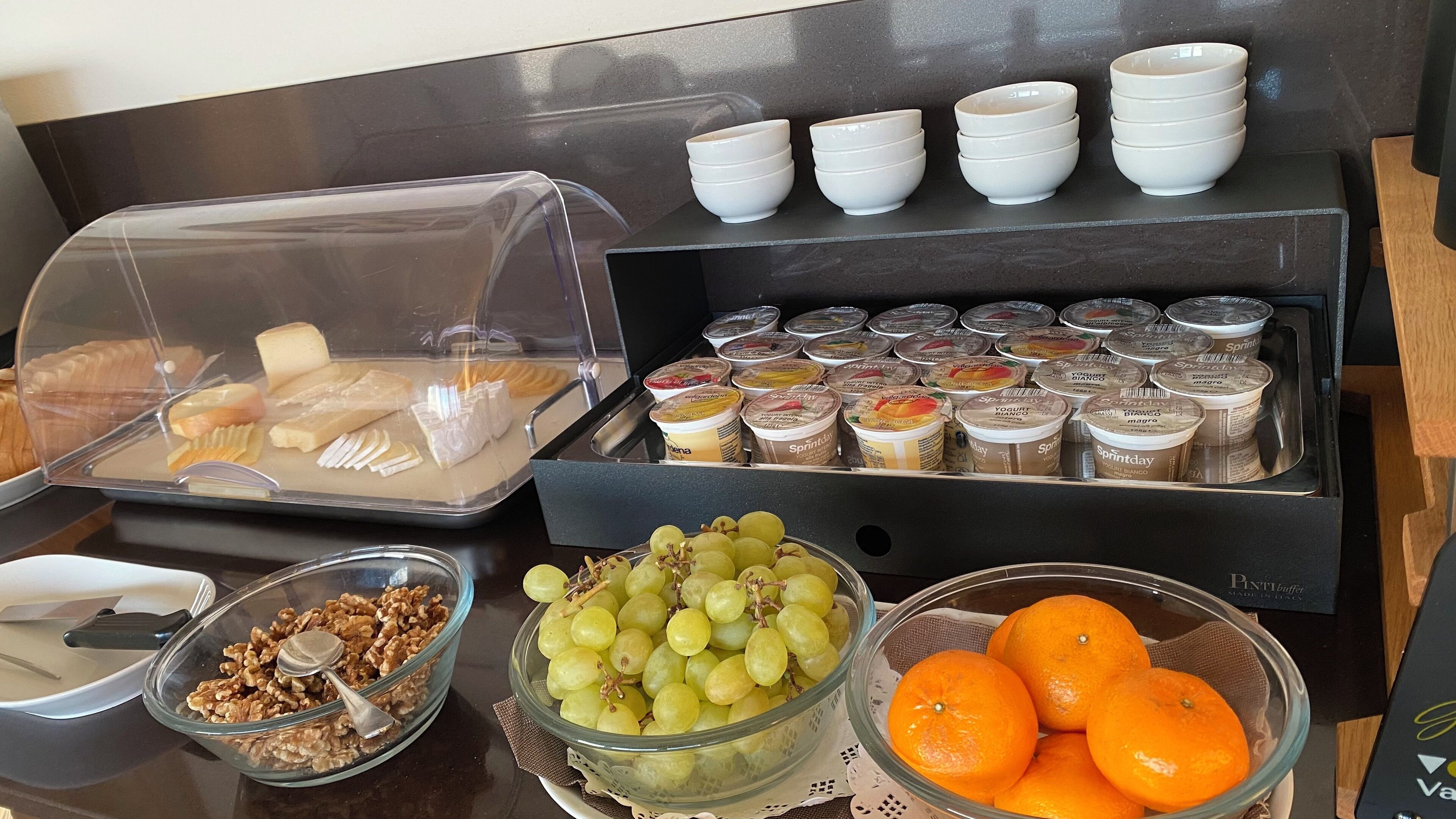 Un bufé de desayuno con diversas opciones de comida, incluyendo yogur, frutas y bollería.