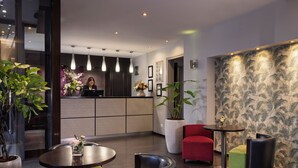 A modern lobby with a reception desk, seating area, and decorative plants. - Jack's Hotel (Paris)
