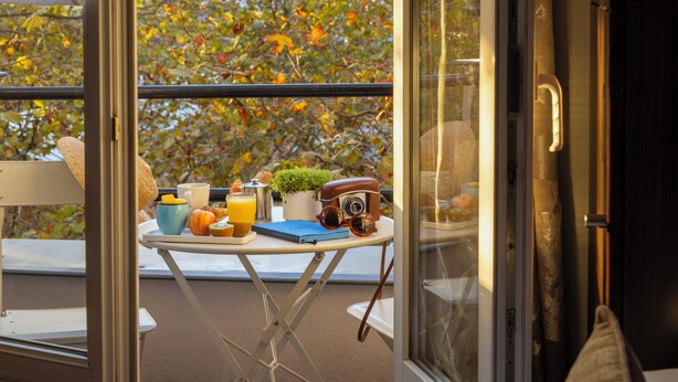 A balcony with a table set for breakfast, including a camera, a plant, and various breakfast items. - Jack's Hotel (Paris)