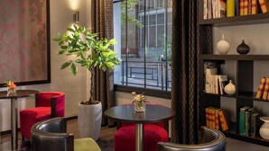 A modern interior with a round table, red chairs, a large potted plant, and a bookshelf with books and decorative items. - Jack's Hotel (Paris)