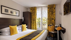 A hotel room with a large bed, a desk with a chair, a small table with a coffee maker, and a view of the outdoors through the window. - Jack's Hotel (Paris)