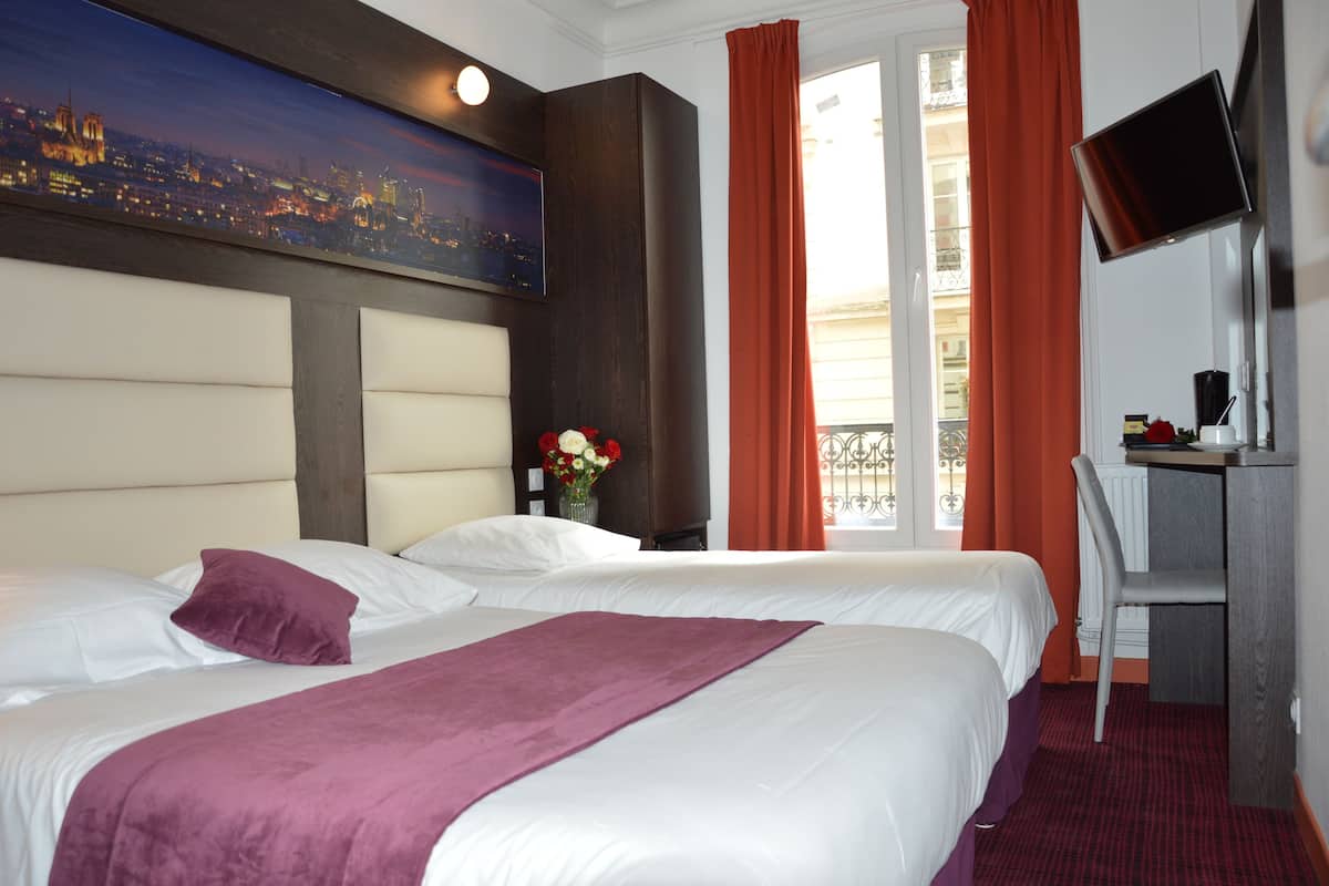 A hotel room with two beds, a large cityscape painting on the wall, a desk with a chair, and a TV mounted on the wall.