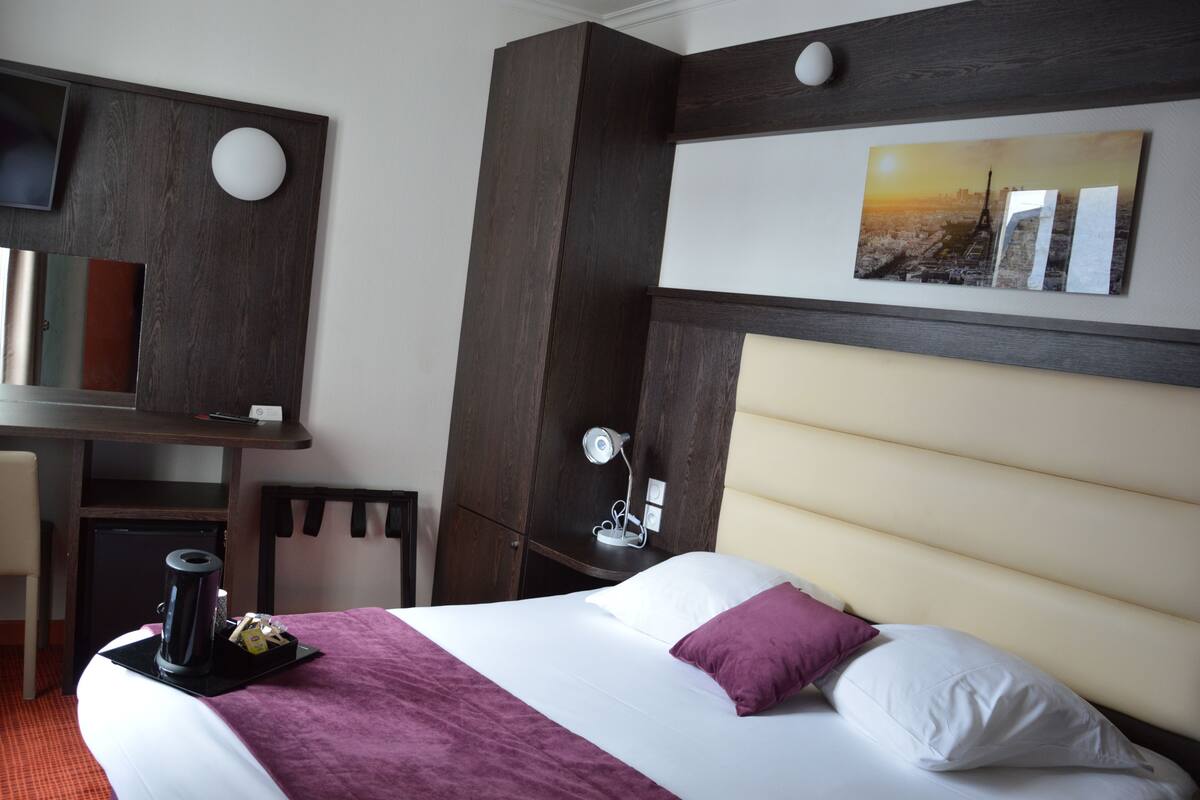 A hotel room with a bed, bedside table, lamp, and a desk with a chair.