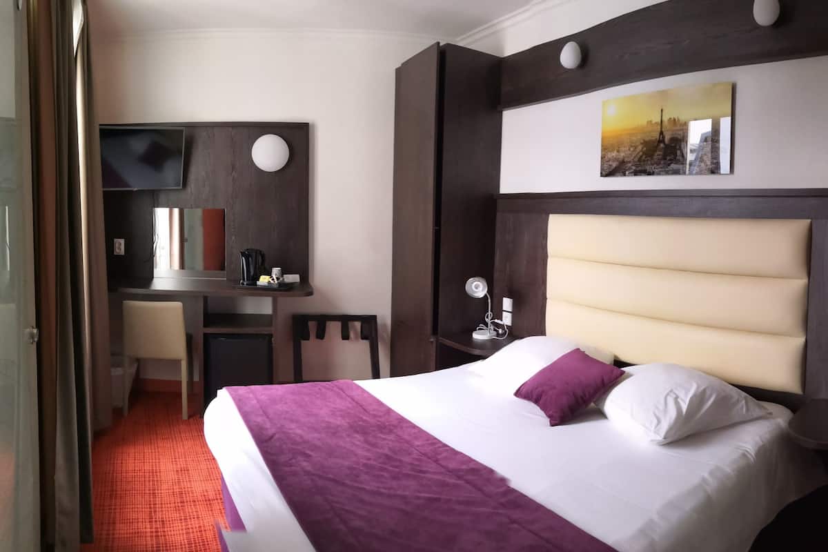 A hotel room with a bed, a desk, a chair, a TV, and a painting on the wall.