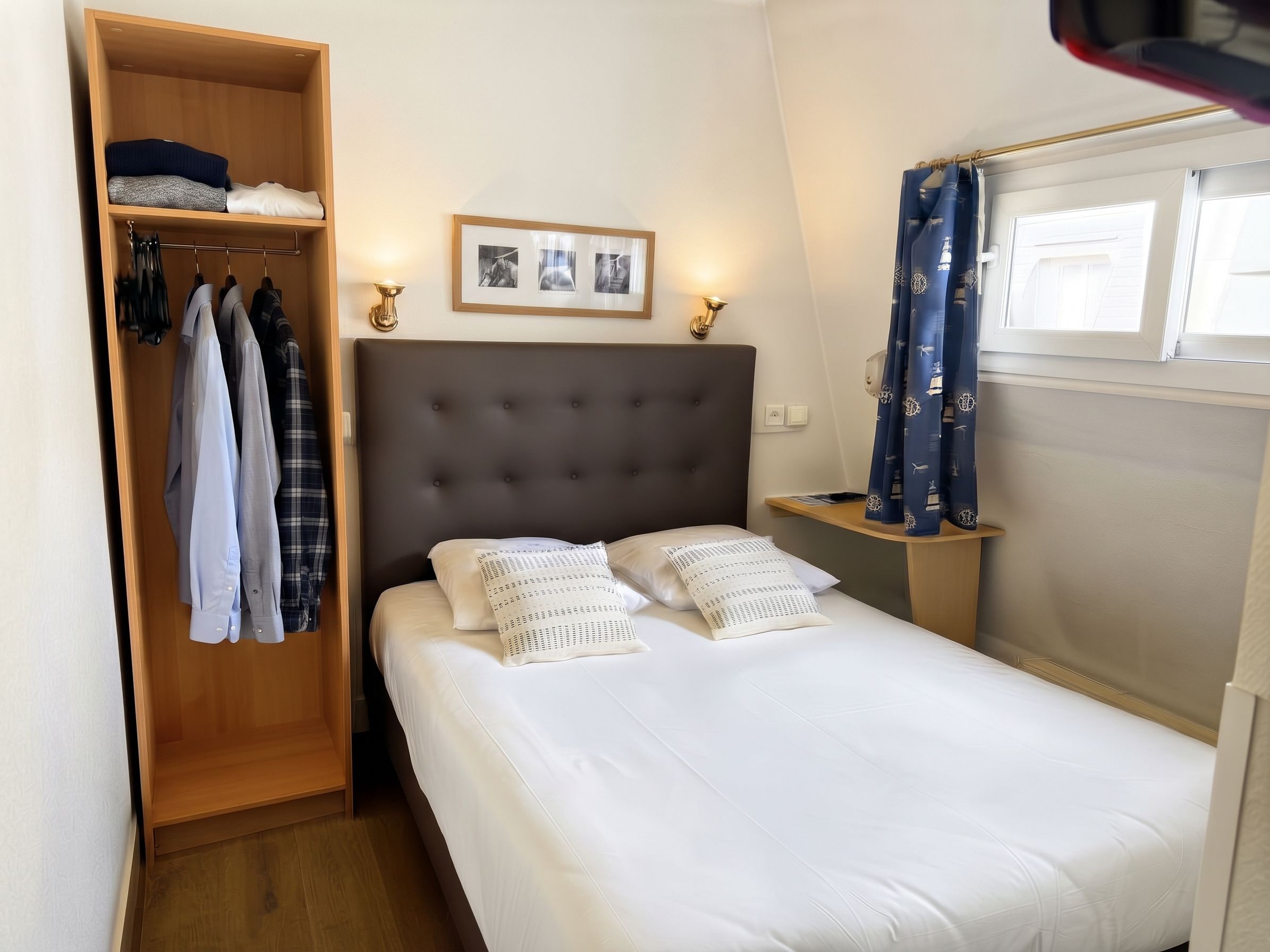 A hotel room with a bed, a wardrobe, a bedside table, and a window with curtains.