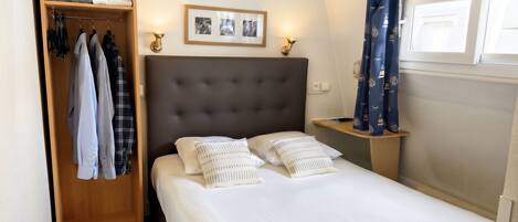 A hotel room with a bed, a wardrobe, a bedside table, and a window with curtains.