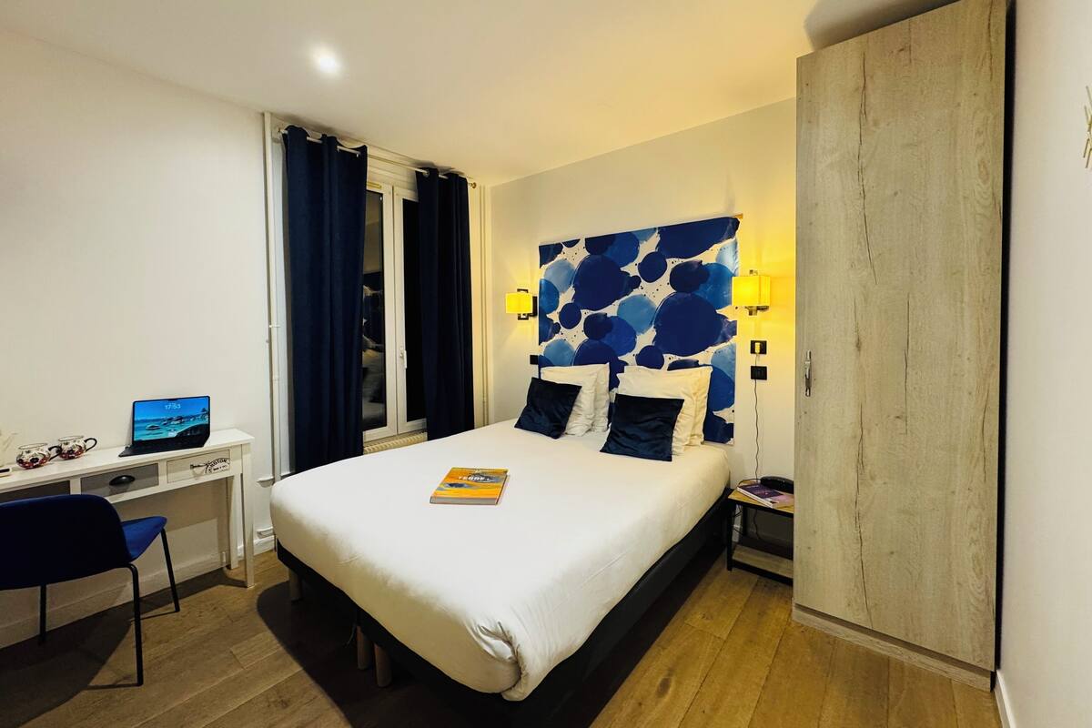 Une chambre d’hôtel équipée d’un lit, d’un bureau, d’une chaise, d’une armoire et d’une fenêtre avec des rideaux.