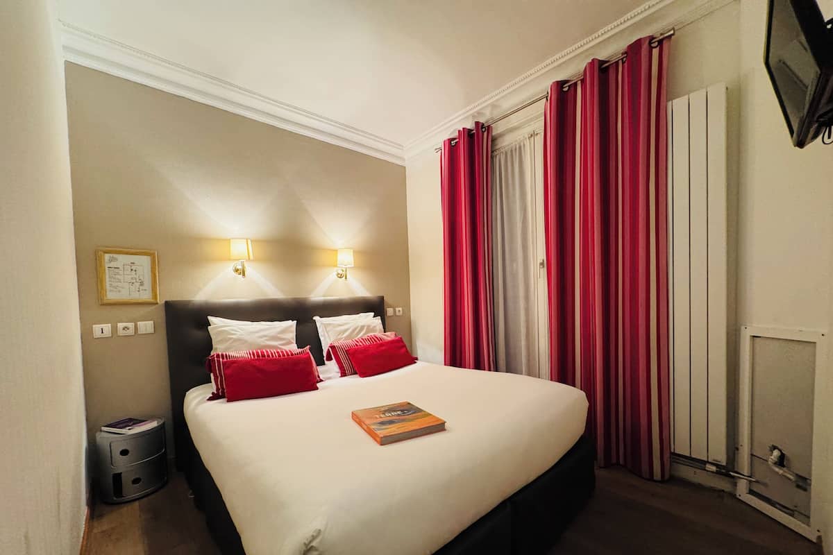 Une chambre d’hôtel avec un grand lit, deux lampes de chevet, une table de nuit et une fenêtre avec des rideaux rouges.