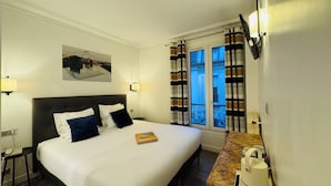A hotel room with a large bed, a bedside table with a lamp, a small table with a kettle, and a window with curtains. - Amiral (Paris)