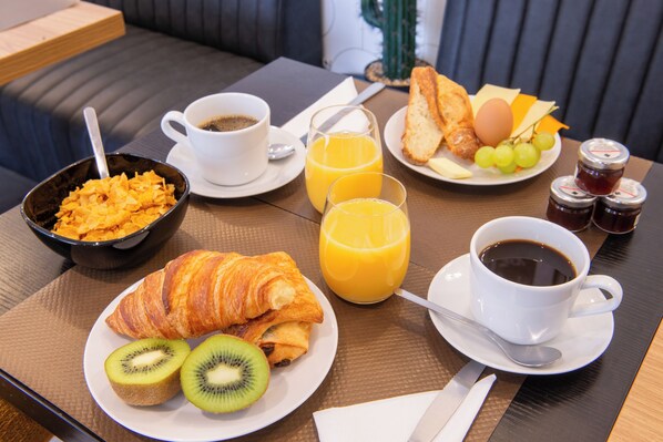 A breakfast table with croissants, kiwi slices, orange juice, coffee, toast, eggs, and jam.