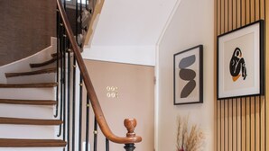 Una escalera de madera con barandilla negra y un jarrón con plantas secas en el suelo.