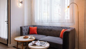 Una sala de estar moderna con un sofá gris, dos cojines naranjas, una mesa de centro redonda y una mesita de lectura con una revista.