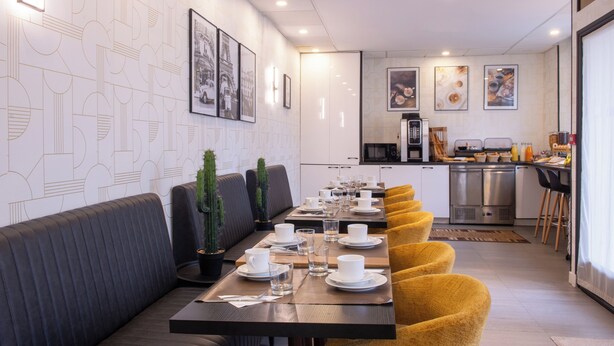 Un comedor moderno con una larga mesa dispuesta para una comida, una cocina al fondo y un muro con estampado.
