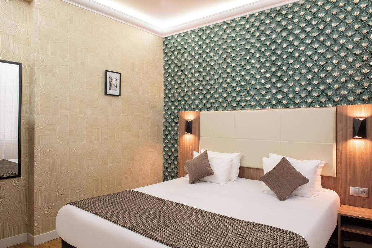 Une chambre d’hôtel avec un grand lit, une tête de lit et un mur orné d’un motif géométrique.