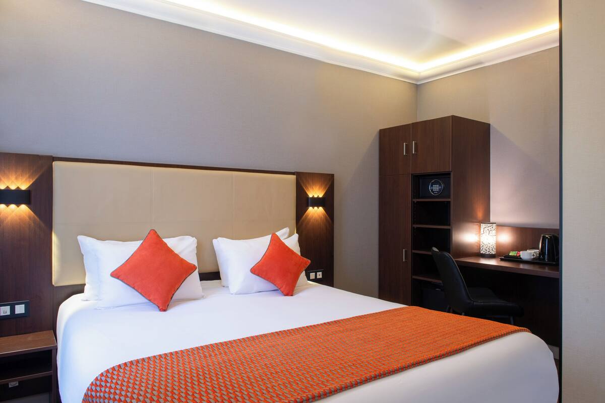 Une chambre d’hôtel avec un grand lit, deux oreillers, un bureau avec une chaise et une lampe.