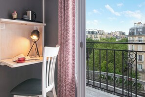 A balcony with a view of Parisian buildings, a white chair, a desk with a lamp, and a red cup. - Hôtel Baldi by Magna Arbor (Paris)