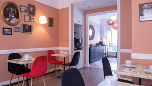 Un comedor con sillas rojas y negras, una mesa dispuesta con vajilla blanca y cuadros en la pared.