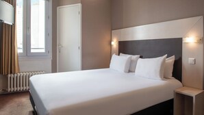 Una habitación de hotel con una cama grande, una mesita de noche, una lámpara de pared y una ventana con cortinas.