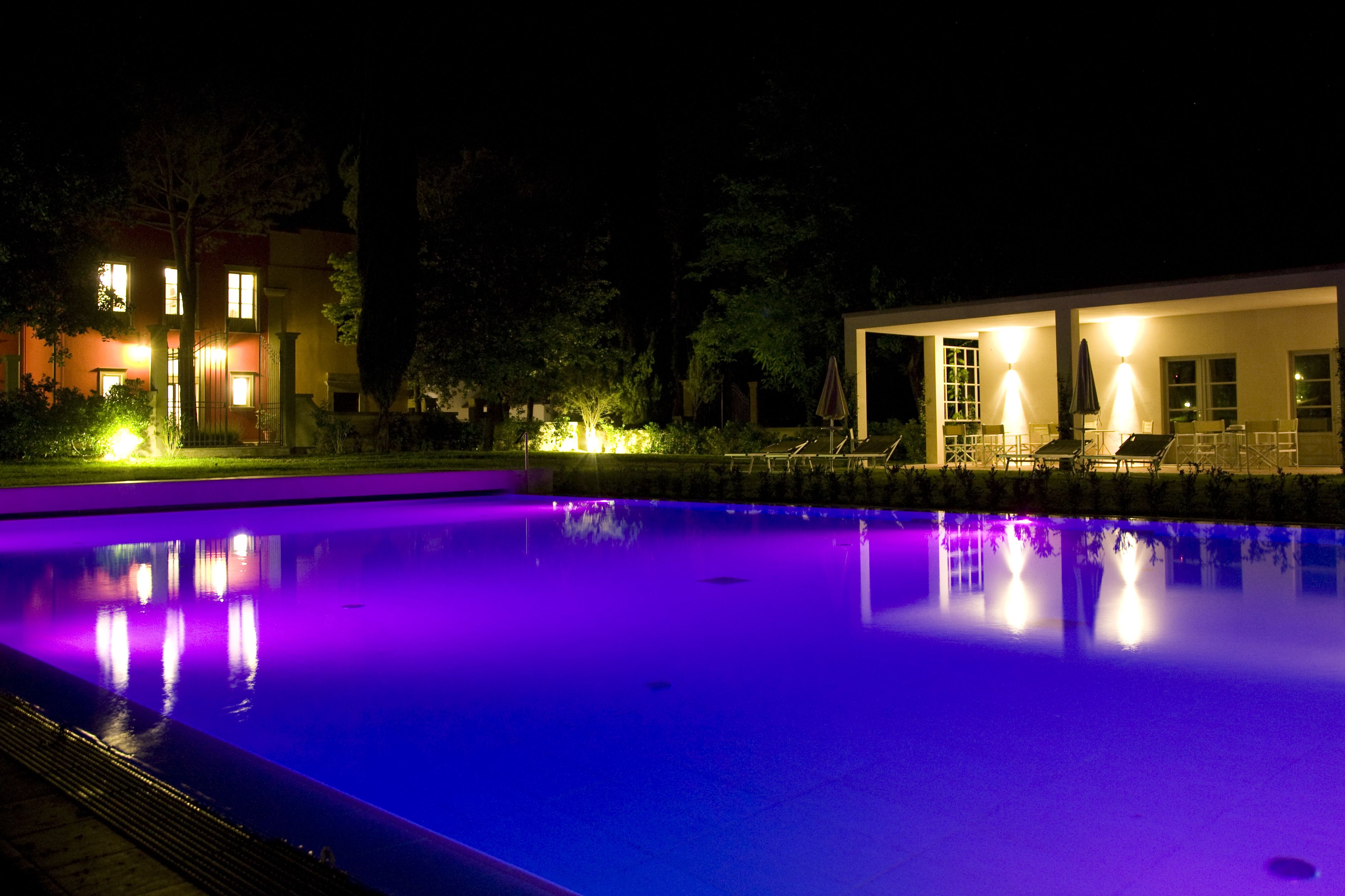 A swimming pool at night with surrounding buildings and outdoor seating.