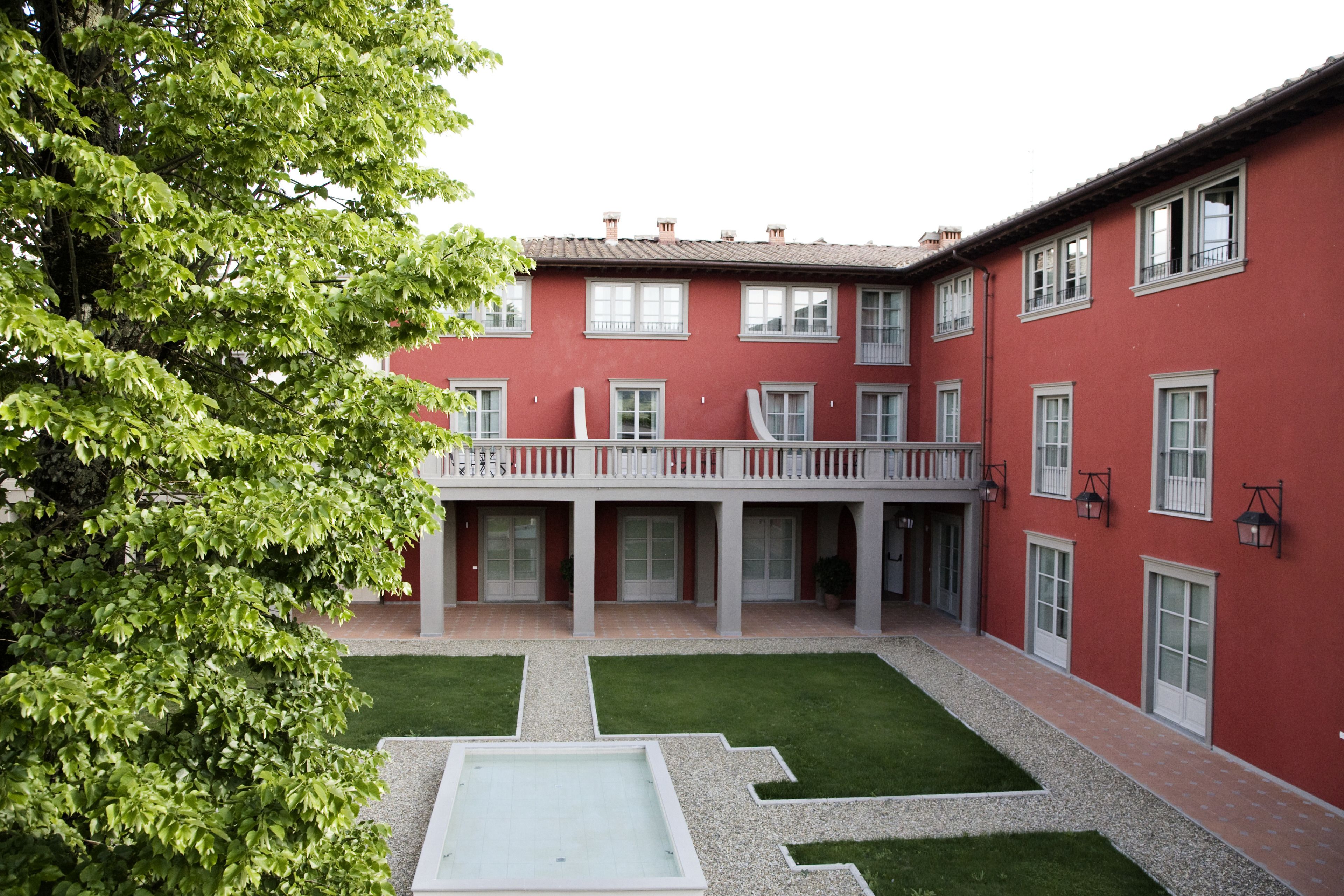 A courtyard with a red building, a white balcony, and a tree.