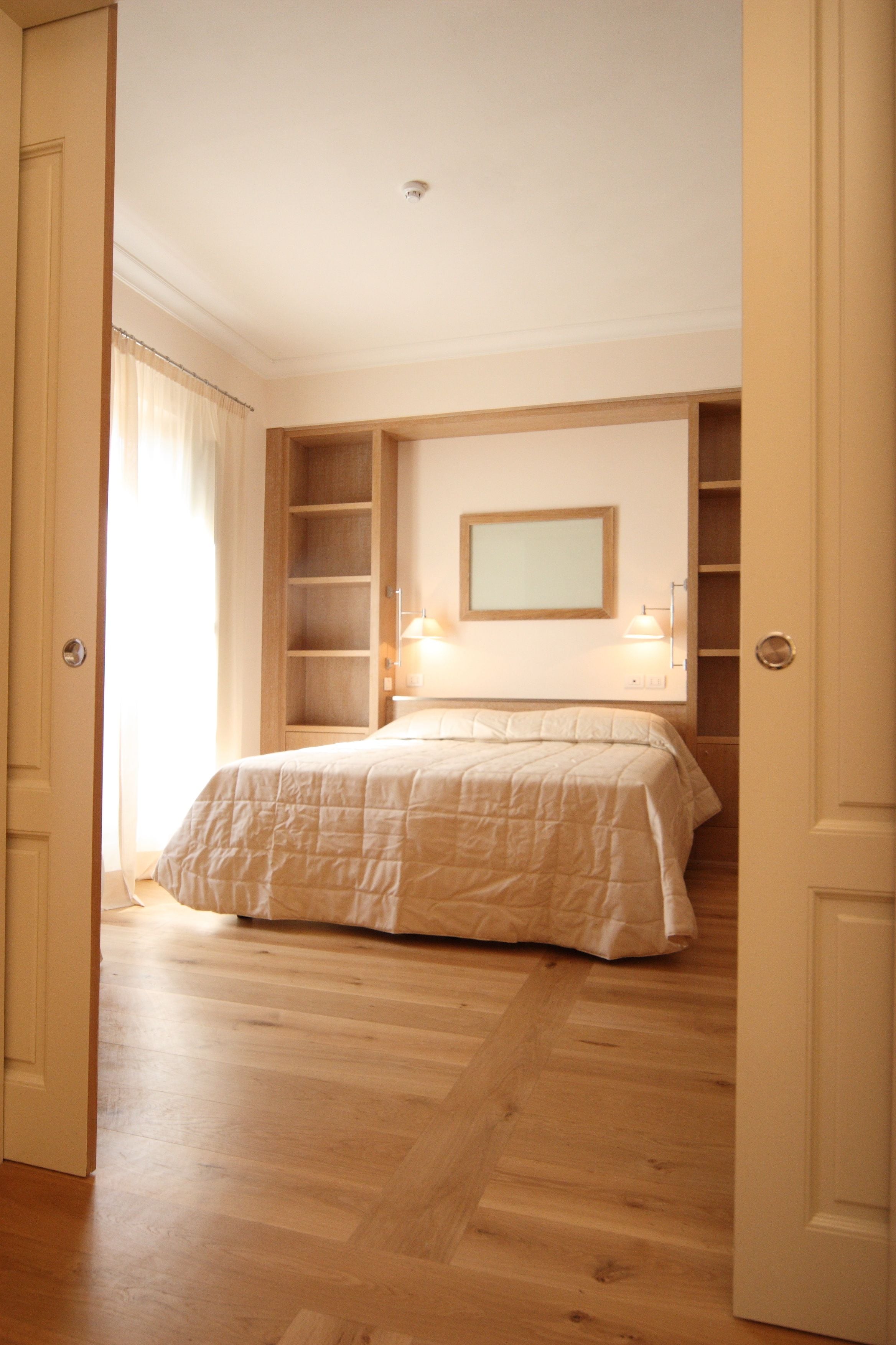 A bedroom with a bed, a nightstand, a mirror, and built-in shelving.