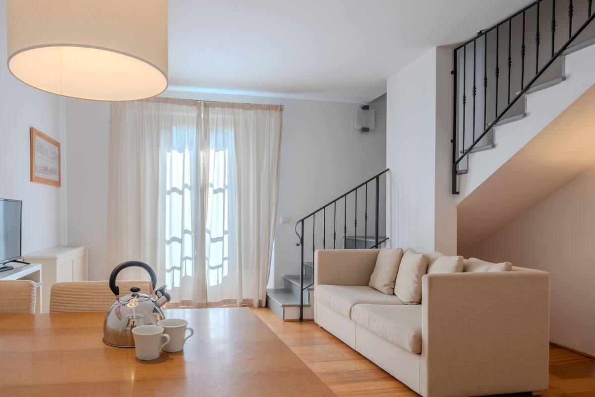 Una sala de estar moderna con un sof á, una mesa con una tetera y tazas, una escalera y un televisor sobre un mueble.