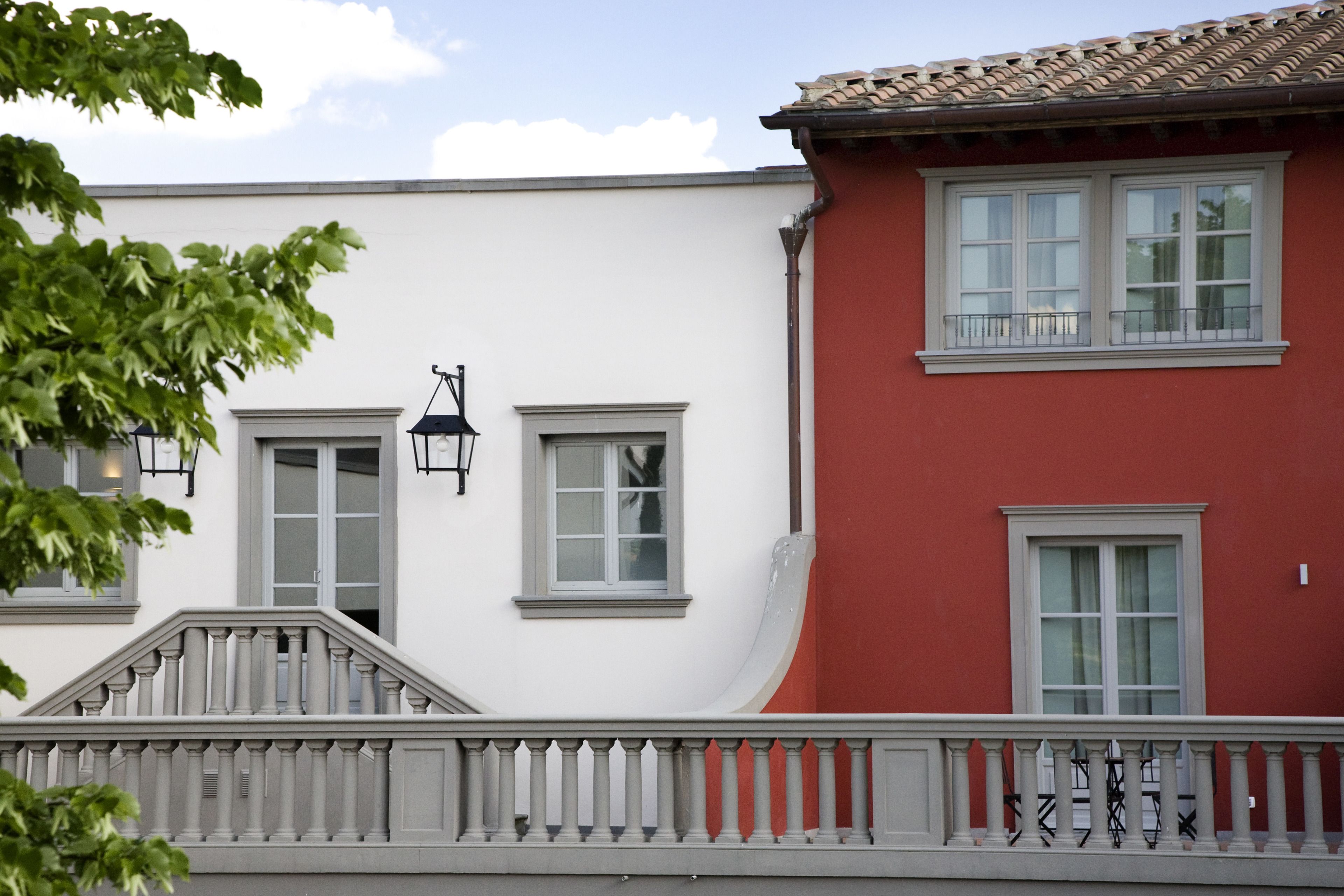 Ein Gebäude mit weißer und roter Fassade, zahlreichen Fenstern und einem Balkon mit Brüstung.
